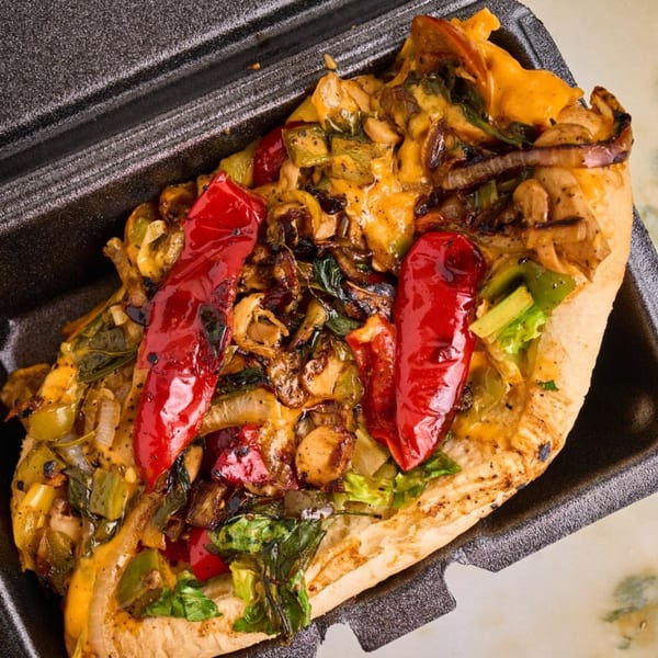 A VeggieBusters cheesesteak with grilled red peppers, onions, and mushrooms in a black container.