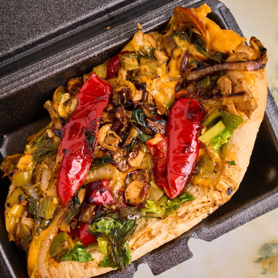 A VeggieBusters cheesesteak with grilled red peppers, onions, and mushrooms in a black container.