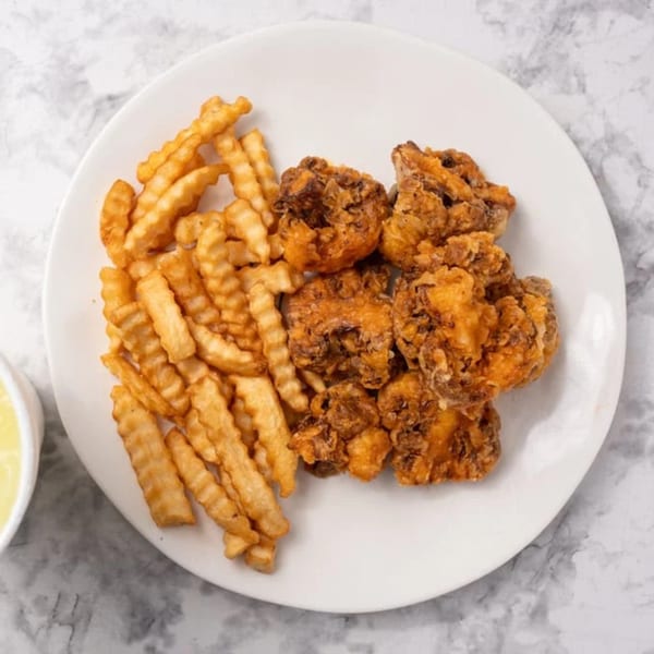 A white plate holds crispy fried chicken pieces and crinkle-cut fries, with a side of dipping sauce.