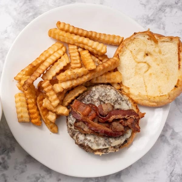 A GutBusters bacon cheeseburger with melted cheese and crinkle-cut fries on a white plate.