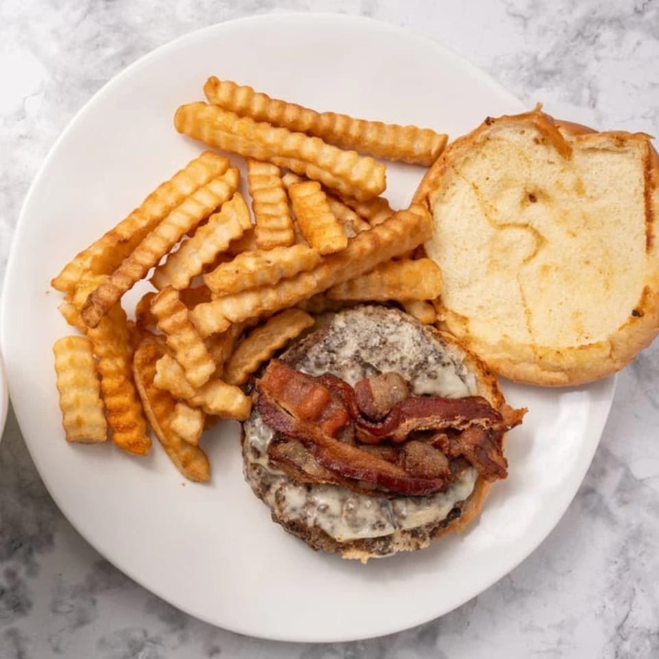 A GutBusters bacon cheeseburger with melted cheese and crinkle-cut fries on a white plate.