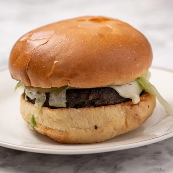 A close-up of a VeggieBusters veggie burger with melted cheese and shredded lettuce on a bun.