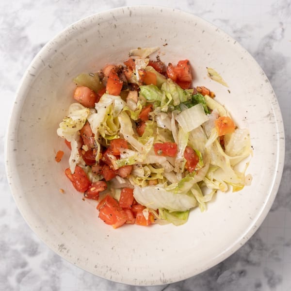 A white bowl filled with a simple salad of chopped lettuce and diced tomatoes, seasoned with pepper.