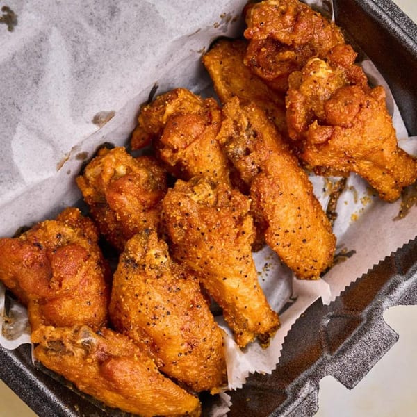 Crispy, golden-brown chicken wings seasoned with black pepper, served in a black takeout container.